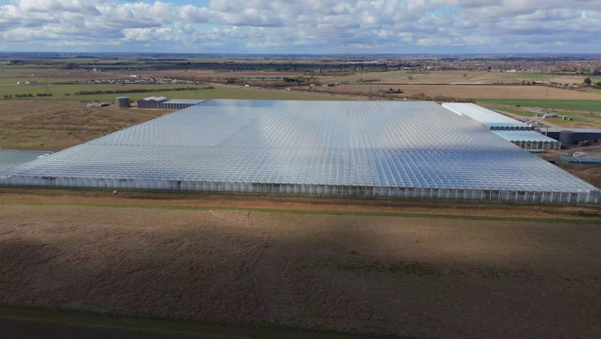 Aerial view of large data centre processing facility glass building expansive countryside flat agricultural land quantum farming sunny day England UK Europe.