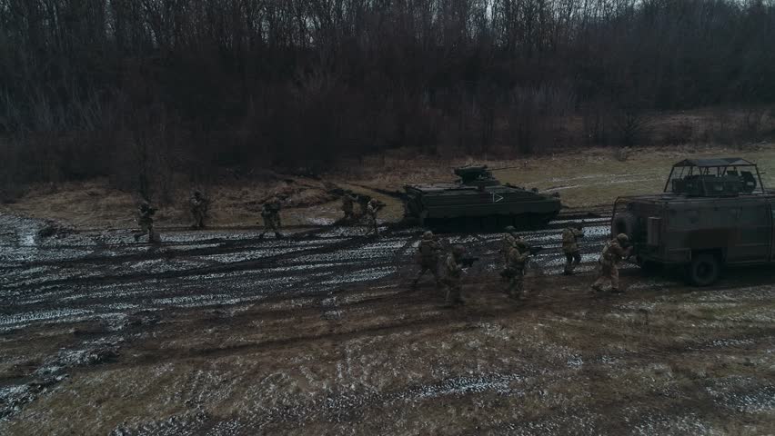 military personnel move together with armored vehicles