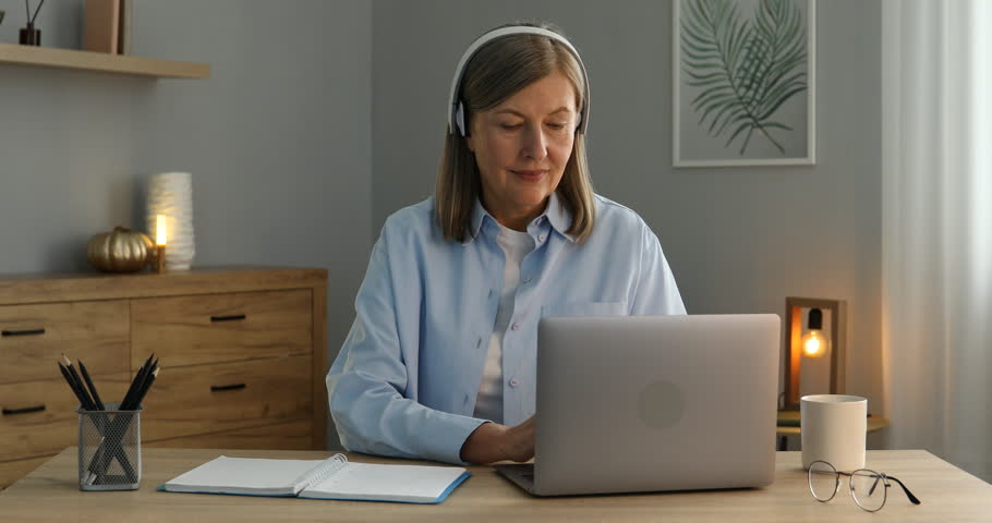 Smiling woman learning online using laptop and taking notes at table indoors. Self-study