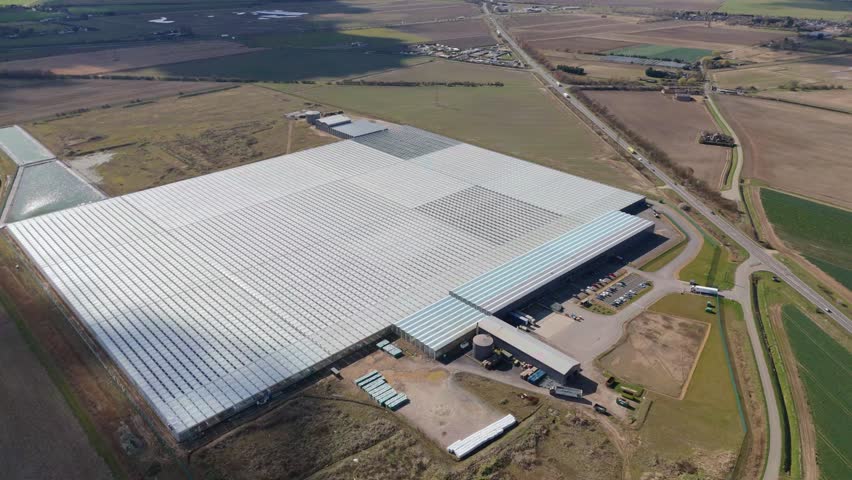 Aerial view of large data centre processing facility glass building expansive countryside flat agricultural land quantum farming sunny day England UK Europe.