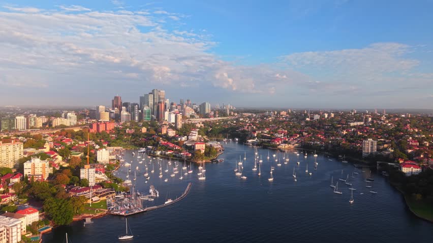 Drone establishing overview of Neutral Bay, stunning sailboats anchored below Sydney skyline and waterfront