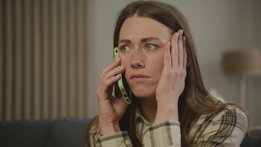 Stressed woman receiving bad news on phone, holding head in frustration at Home