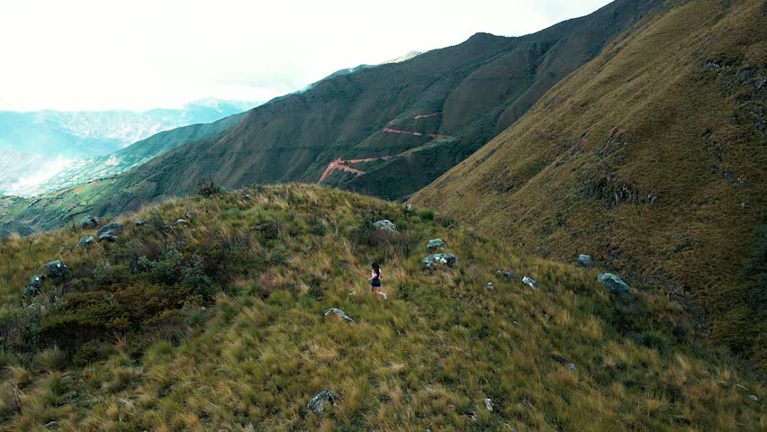 Young woman running in nature among mountains and magical landscapes. Girl in shorts enjoying the outdoors and mountain tourism. Healthy lifestyle. Drone video.
