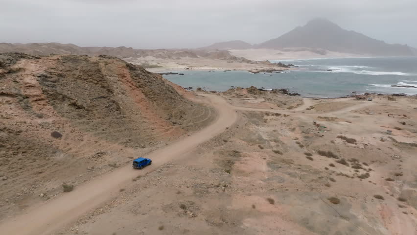 Winding coastal road through rugged terrain with a blue car on a scenic drive