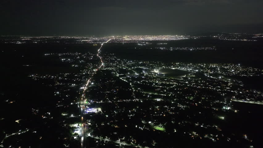 Aerial night flight over Bishkek suburb, illuminated roads leading to city, scattered lights, dark sky, urban-rural transition, smooth, no movement.