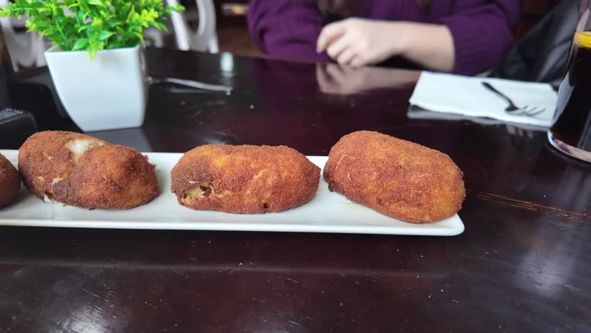 closeup view of the hand of a young white woman picking up a Spanish traditional croquette to eat it.