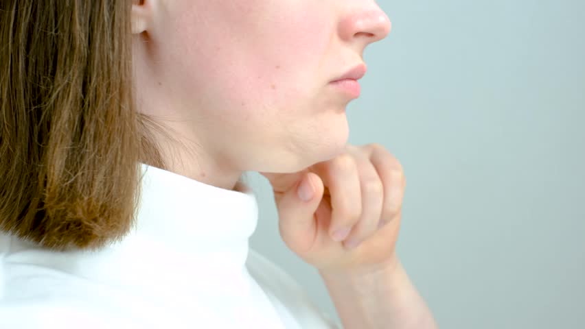Female face with double chin close-up on gray background, side view.