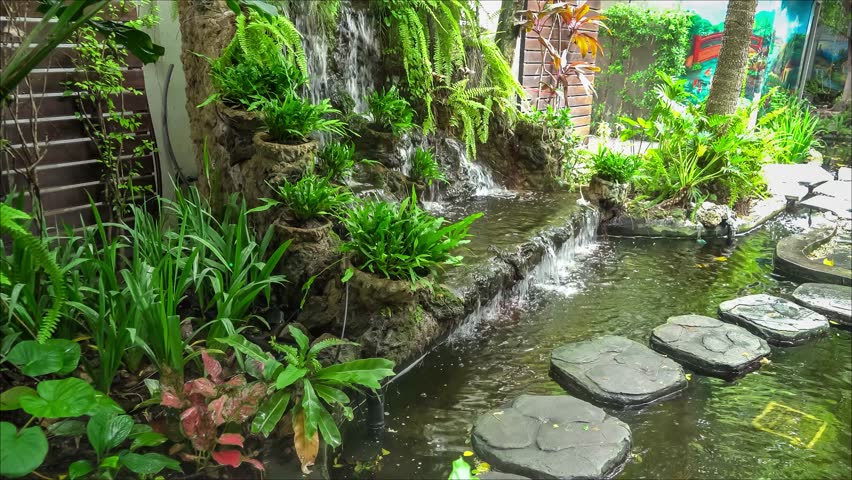 Tranquil garden scene with lush greenery, a small waterfall flowing into a pond, and stepping stones crossing the water