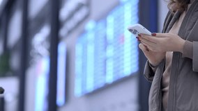Woman is looking at her phone in a busy airport. The background is filled with multiple screens displaying flight information. The woman is focused on her phone - Powered by Shutterstock - Get 15% off with code: PIKWIZARD15
