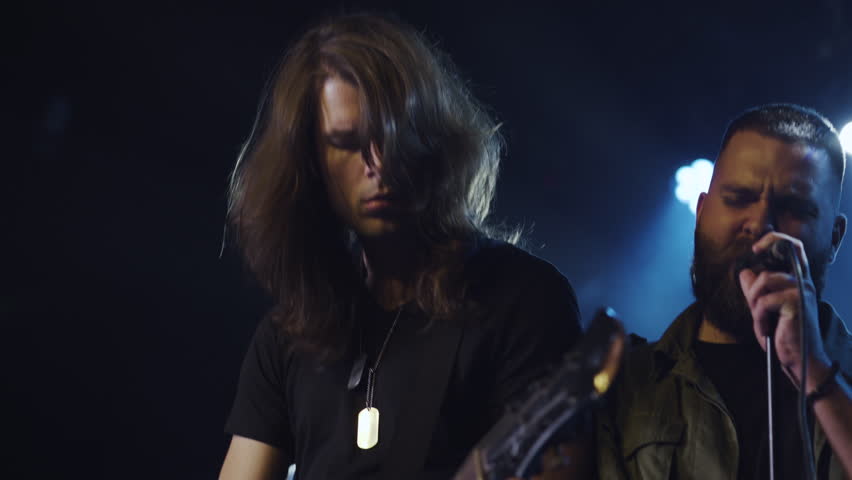 Energetic musicians playing guitars and singing in a captivating slow motion performance under blue stage lights