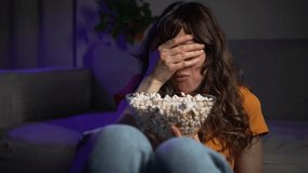 Anxious female tensely nibbling popcorn, reacting dramatically to scary movie playing on tv screen, displaying wide-ranging fear responses during solitary nighttime viewing - Powered by Shutterstock - Get 15% off with code: PIKWIZARD15