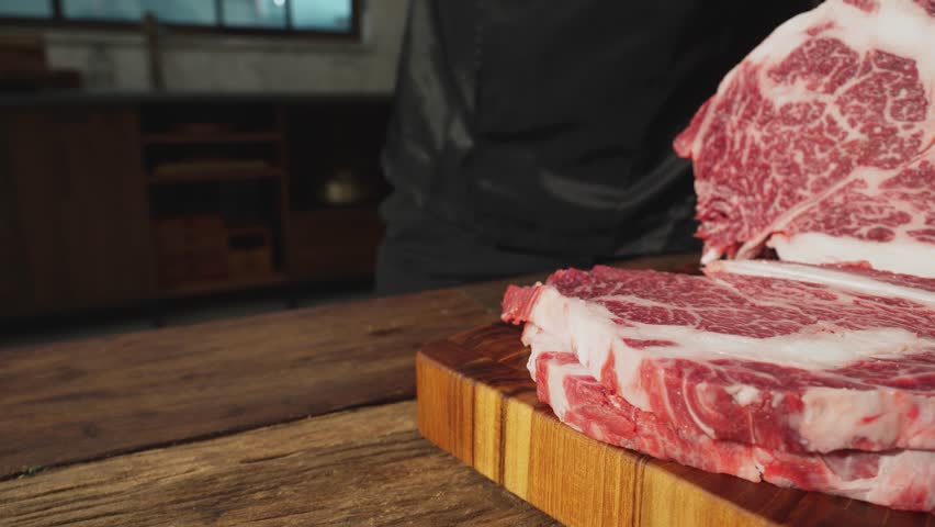 They are cutting raw meat on a wooden cutting board.