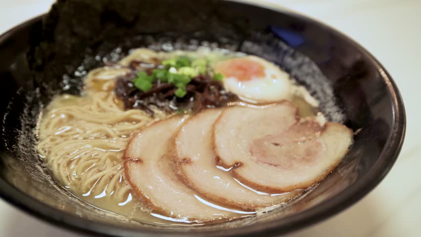 Close-up view of the Japanese ramen soup with chashu pork, egg and fungus on the table.