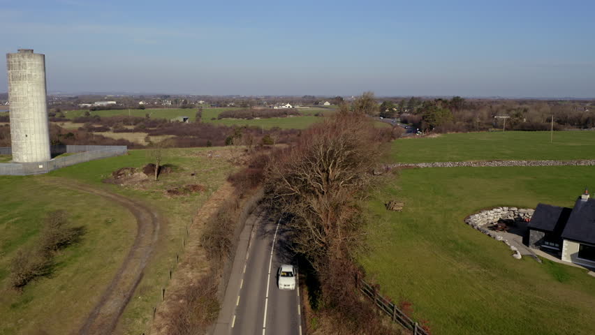 Aerial tracking shot over a country road in Galway, Ireland, gliding above roadside trees on a sunny day
