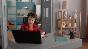 Cute smart teenage African American boy in wireless headphones e-learning using laptop pc, studying online lesson and writing assignment into exercise book in domestic room. - Powered by Shutterstock - Get 15% off with code: PIKWIZARD15