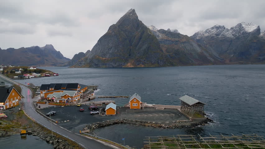The famous yellow house in Reine, Lofoten Islands, Norway, with a dramatic mountain backdrop, aerial orbit right
