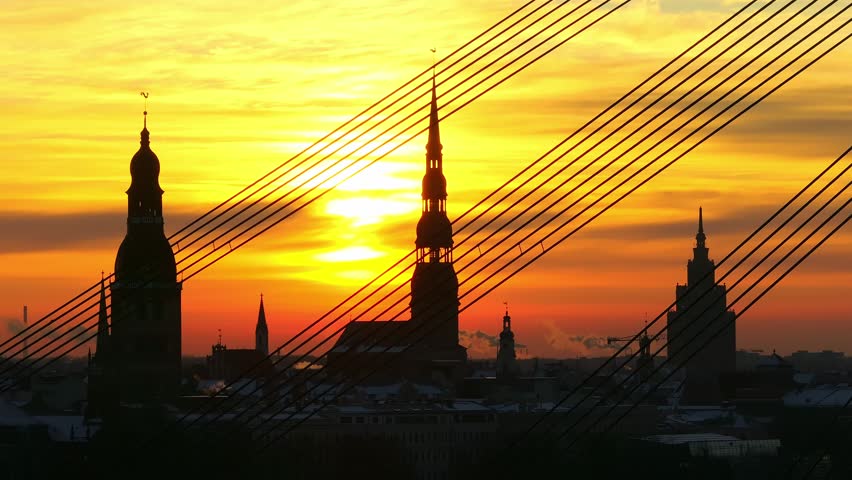 Silhouetted Riga skyline at sunrise with structured bridge cable lines, Drone