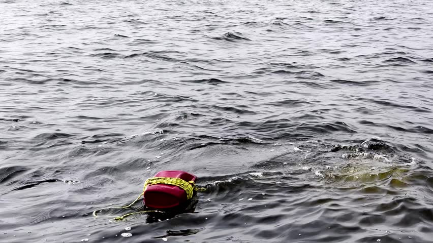 low-angle, wide shot of a red buoy with yellow rope floating in the dark, choppy Baltic Sea