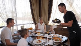 The waiter puts plates with various dishes at breakfast in the restaurant for a large family with children.  - Powered by Shutterstock - Get 15% off with code: PIKWIZARD15