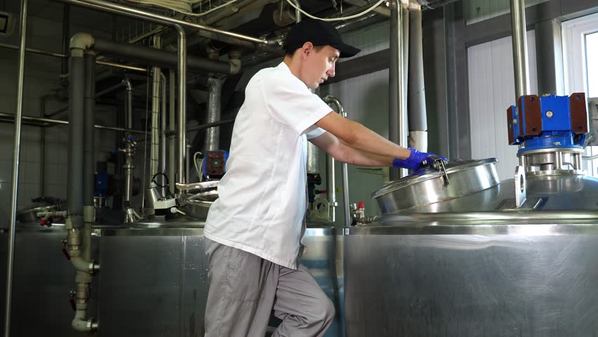 The process of producing various varieties of cheese on a dairy farm. A man in uniform shows the work of modern equipment. Dairy factory, cheese factory.