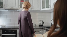Close-up rear view of woman reading novel at home while her mother walks into the kitchen, looking at her with a warm smile, creating a cozy and intimate family moment in a modern home setting - Powered by Shutterstock - Get 15% off with code: PIKWIZARD15