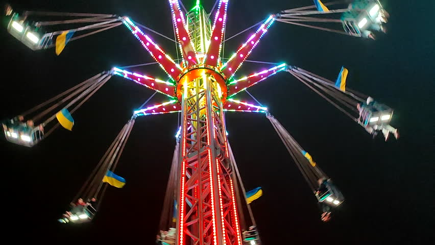 Amusement attraction in an amusement park at night. Amusement park ride at night. Lots of people relaxing at the attraction. Amusement ride with glowing multi-colored illumination backlight