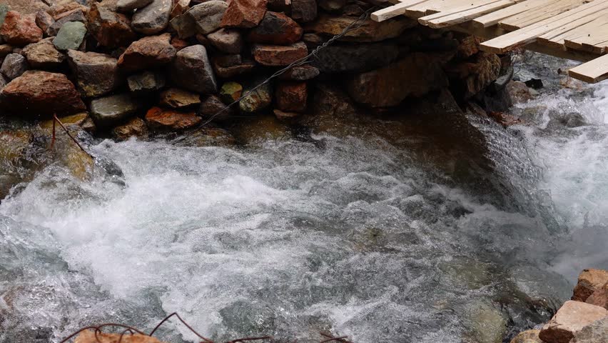 A clear stream flows towards the river under a small bridge in Zanskar, Ladakh.