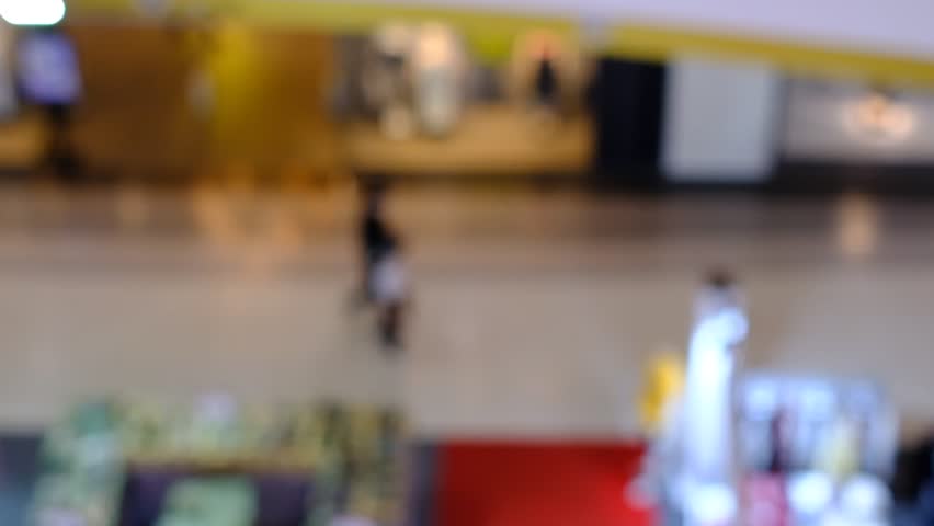 A blurry image of a shopping mall with people walking around. Scene is busy and bustling, with people going about their day