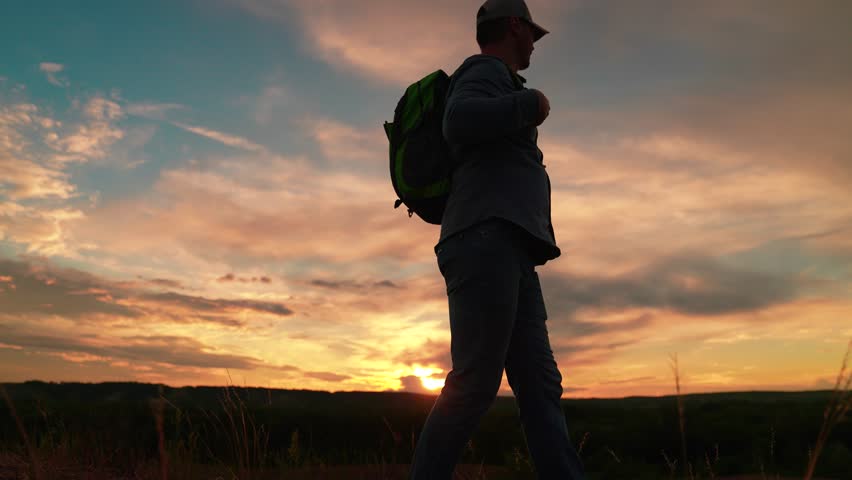 Active hiker man silhouette walking on meadow sunset epic bright cloud sky. Travel freedom man backpacker trekking discovery contemplate picturesque sunrise. Hiker man with backpack, sporty lifestyle