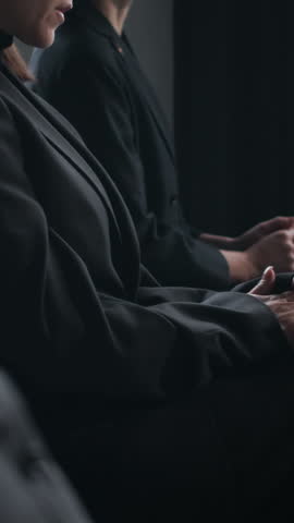 Vertical tilt-up shot of woman covering her face as she crying during memorial service indoors, sitting among other mourners