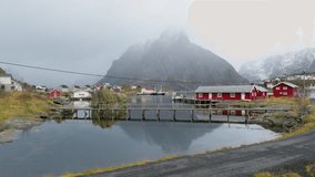 A male photographer with a digital camera in his hand walking over wooden foot bridge, Hammerskaft village, Moskenesveien, Reine, Lofoten Islands, Drone shot - Powered by Shutterstock - Get 15% off with code: PIKWIZARD15
