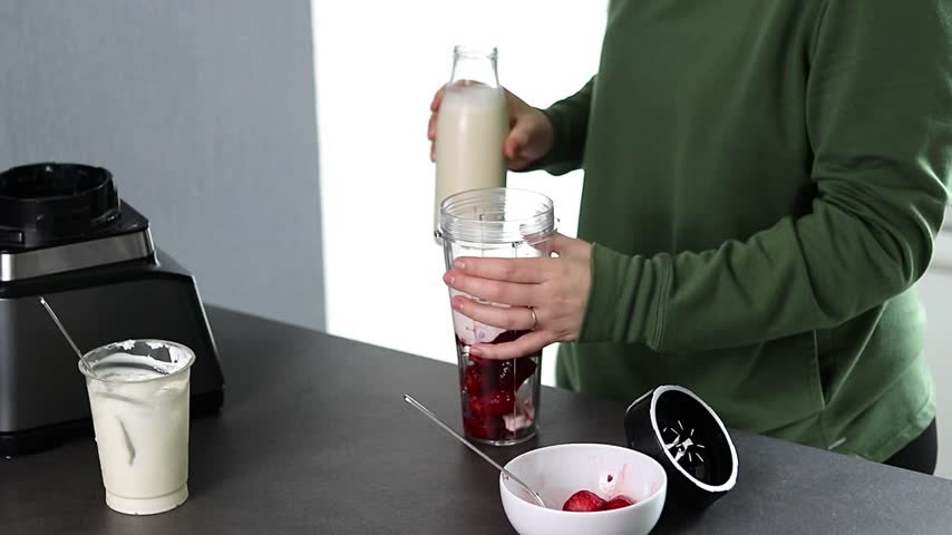 Close up of a woman in green sweater preparing fresh strawberries smoothie with yogurt and milk in the kitchen 