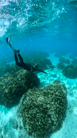 A diver swims underwater near coral formations in Thoddoo, Maldives. Air bubbles rise to the surface as the diver explores the marine environment.