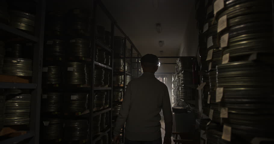 Man Searching for Lost Film Reels in a Dark Archive