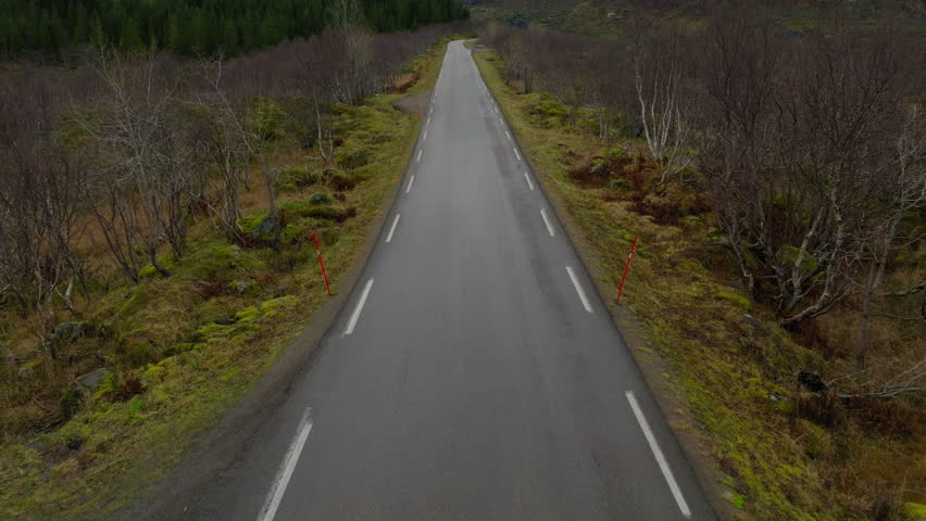 Isolated empty road with snow covered mountains in view in winter, Road to Nusfjord viewpoint, Lofoten islands, Revealing shot