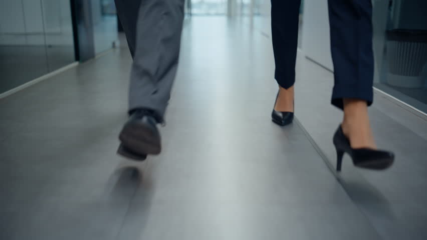 Businesspeople feet walking modern empty corridor closeup. Unrecognizable business colleagues stepping on grey floor hurrying to office work. Elegant pair managers legs strolling corporate vestibule 