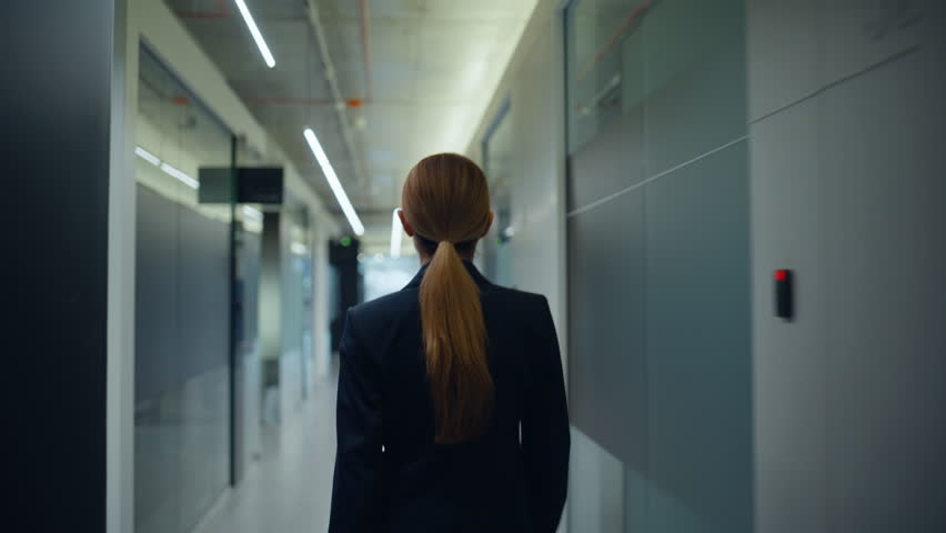 Business lady strolling vestibule alone back view. Blonde relaxed employee woman with ponytail crossing grey corridor rushing on meeting closeup. Calm director in suit stepping at empty building hall