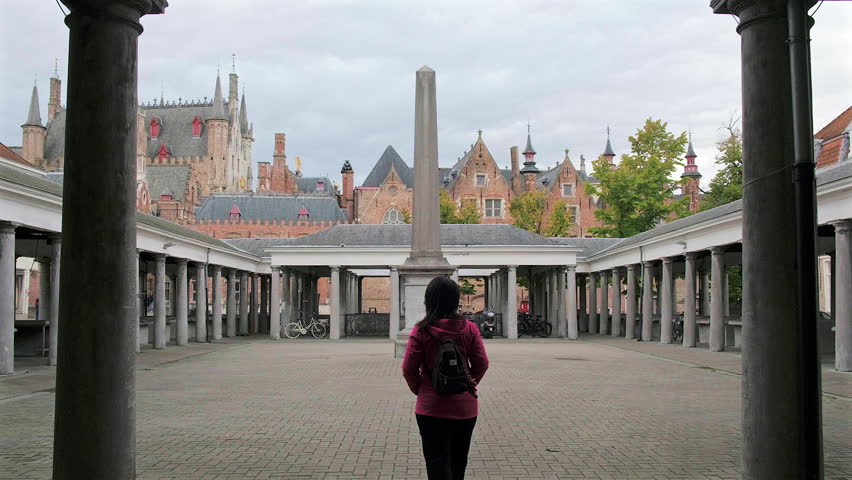 Bruges, Belgium - September 24 2024: Female tourist walking into historic Vismarkt or Fish Market looking at the lovely Stadhuis Brugge view
