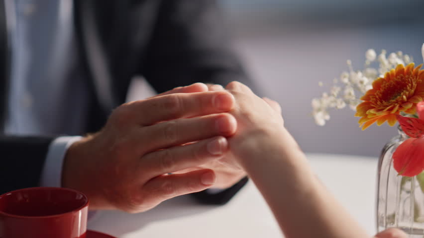 Lovers hands holding gently at cafe table under sunlight closeup. Unknown romantic couple bonding at date in modern cafeteria feeling emotional connection. Man fingers caressing delicate woman skin.
