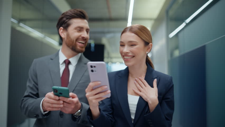 Lady showing smartphone to colleague walking empty hall closeup. Friendly corporate coworkers having work break talking office corridor. Emotional partners looking cellphone together going vestibule - Powered by Shutterstock - Get 15% off with code: PIKWIZARD15