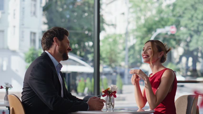 Smiling husband helping wife to sit at modern restaurant. Gallant man flirting with gorgeous woman in red dress spending date in cafeteria. Happy romantic couple laughing enjoy time together in cafe