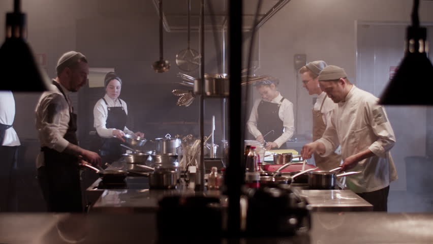 Group of chefs cooking food together in kitchen