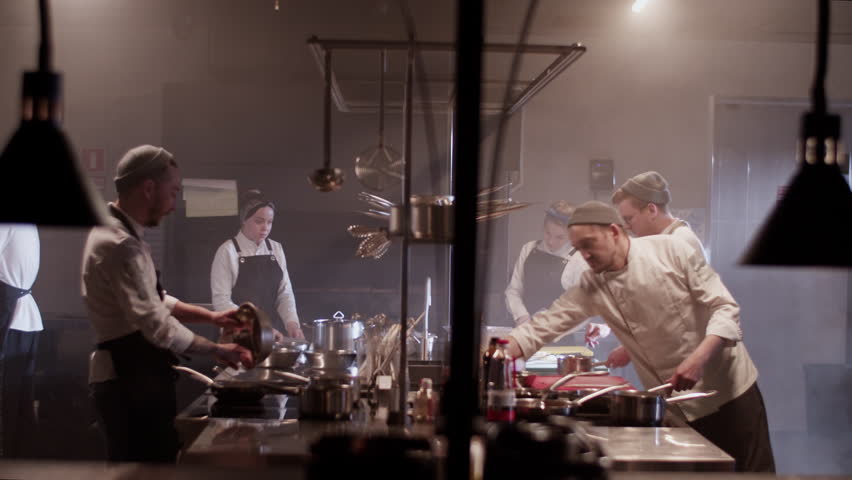Group of chefs cooking food together in kitchen