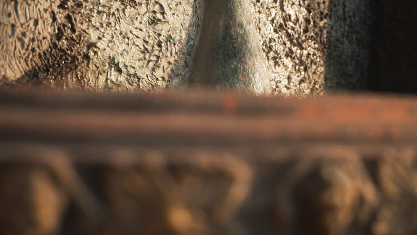 Small decorative antique wall fountain waterfall. Cinematic slow motion of water drops at sunset 