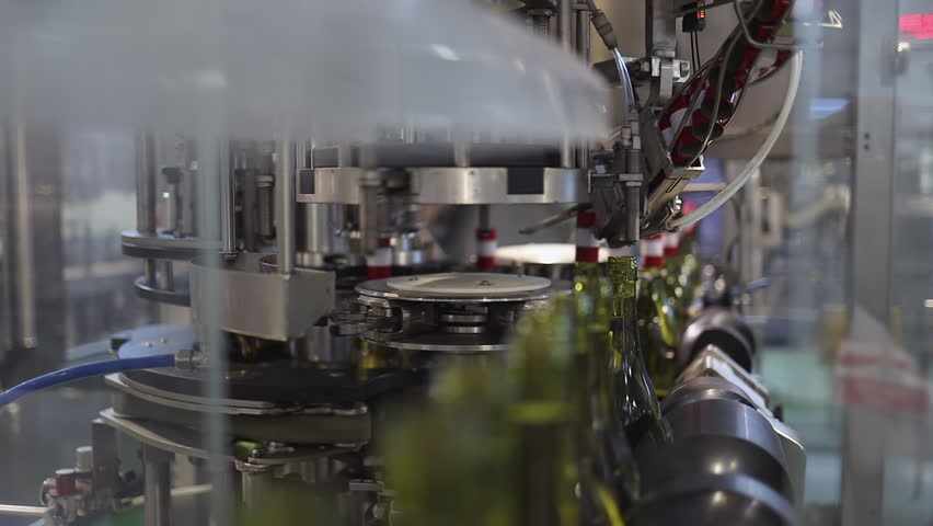Green bottles of white wine on automated line enter neck label station