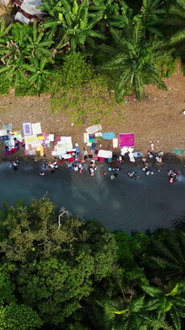 Vertical drone shot above women washing clothes in a river, sunny day in Africa