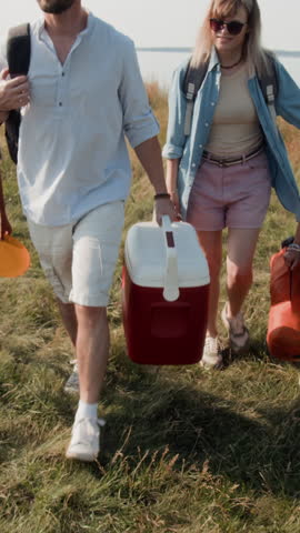 Vertical shot of family walking to car, loading belongings into trunk while leaving sunny lakeshore after camping trip