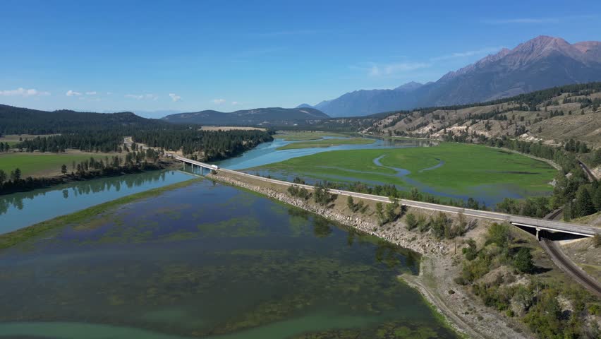 Aerial View of Columbia River Wetlands, Highway, Bridge, and Rocky Mountains on Sunny Day