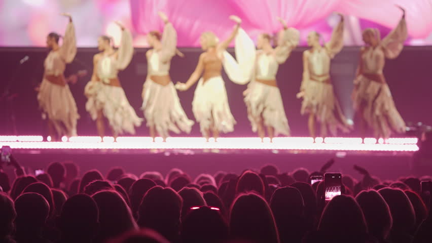 Woman singer sing song on scene. Many female dancers performance. Fun dance music concert. Cool fans people cheering. Lot joy girls moving on stage hall. Epic night live show. Folk artists party fest