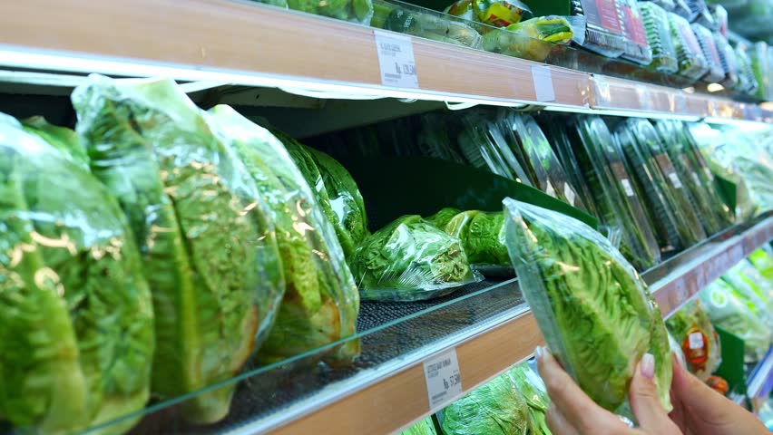 Consumer hand picking fresh salad in store facing plastic wrap dilemma Salad in plastic packaging raises environmental concerns Salad choice reflects conflict between convenience and sustainability
